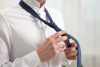 Photo of Man tying stylish necktie at home, closeup