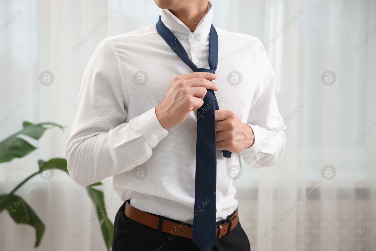 Man tying stylish necktie at home, closeup Photo of Man tying stylish necktie at home, closeup