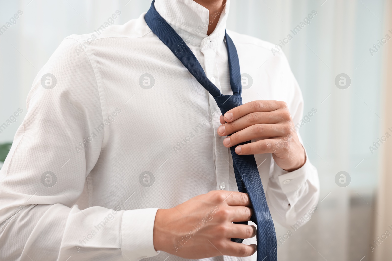 Man tying stylish necktie at home, closeup Photo of Man tying stylish necktie at home, closeup
