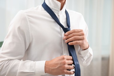 Photo of Man tying stylish necktie at home, closeup
