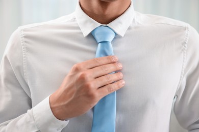 Photo of Man tying stylish necktie at home, closeup