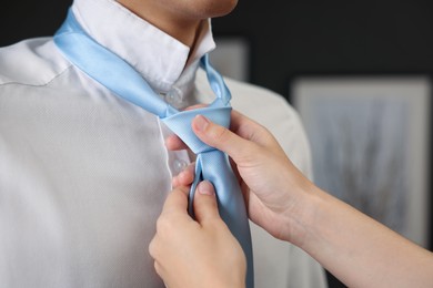 Photo of Woman tying man's necktie at home, closeup