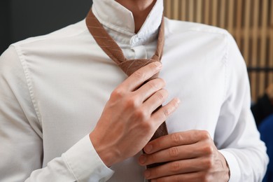 Photo of Man tying stylish necktie at home, closeup