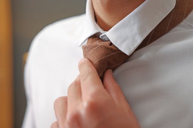 Photo of Man tying stylish necktie at home, closeup