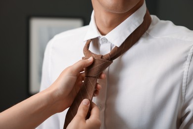 Photo of Woman tying man's necktie at home, closeup