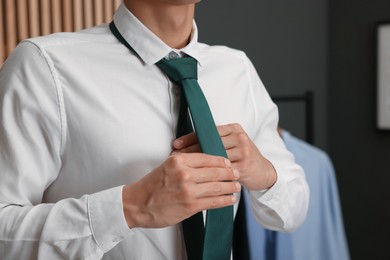 Photo of Man tying stylish necktie at home, closeup