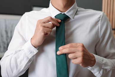 Photo of Man tying stylish necktie at home, closeup