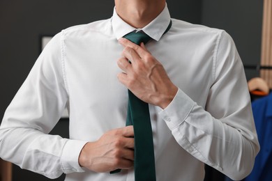 Photo of Man tying stylish necktie at home, closeup