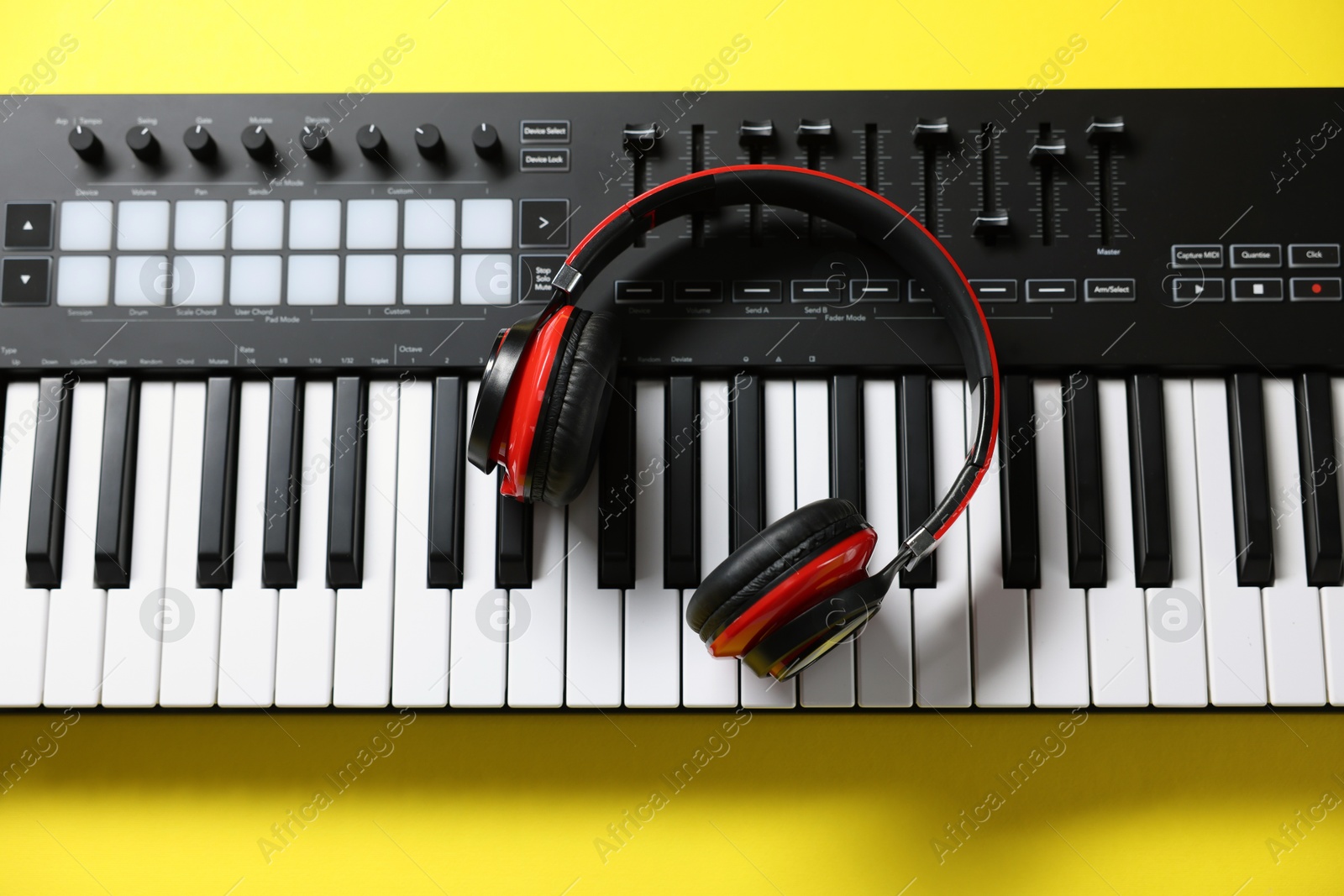 Photo of MIDI keyboard with headphones on yellow background, top view
