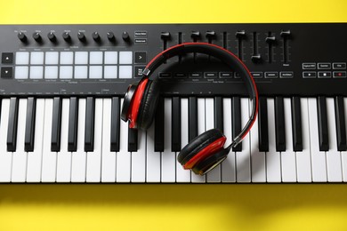 Photo of MIDI keyboard with headphones on yellow background, top view