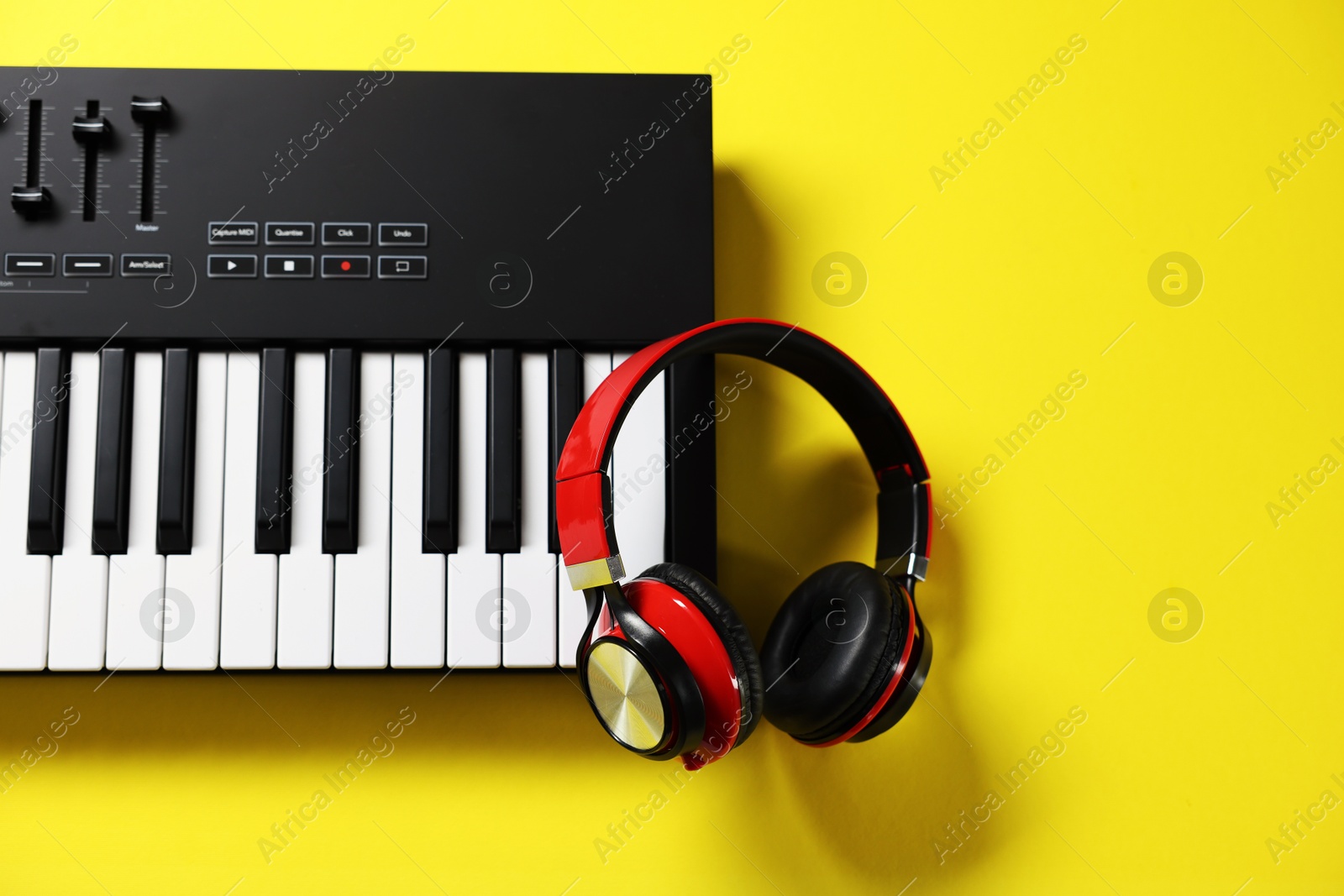 Photo of MIDI keyboard with headphones on yellow background, top view. Space for text