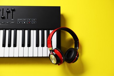 Photo of MIDI keyboard with headphones on yellow background, top view. Space for text