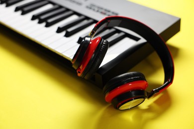 Photo of MIDI keyboard with headphones on yellow background, closeup