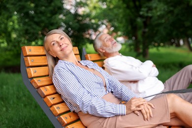 Photo of Lovely senior couple resting on wooden sunbeds in park