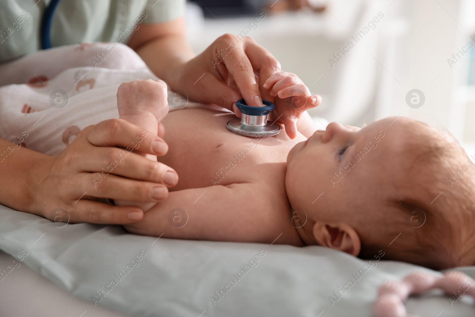 Photo of Pediatrician examining baby with stethoscope at table in clinic, closeup