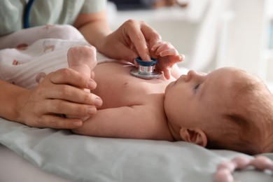 Photo of Pediatrician examining baby with stethoscope at table in clinic, closeup