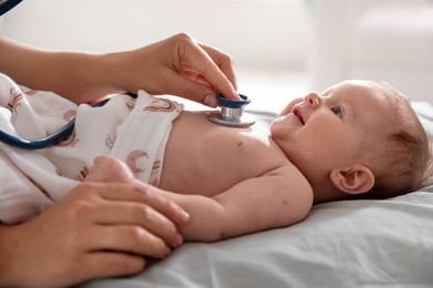 Photo of Pediatrician examining baby with stethoscope at table in clinic, closeup