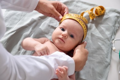 Photo of Pediatrician measuring baby's head with tape at table in clinic, closeup