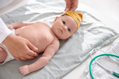 Photo of Pediatrician measuring baby's head with tape at table in clinic, closeup
