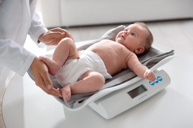 Photo of Pediatrician weighting baby with scales at white table in clinic, closeup