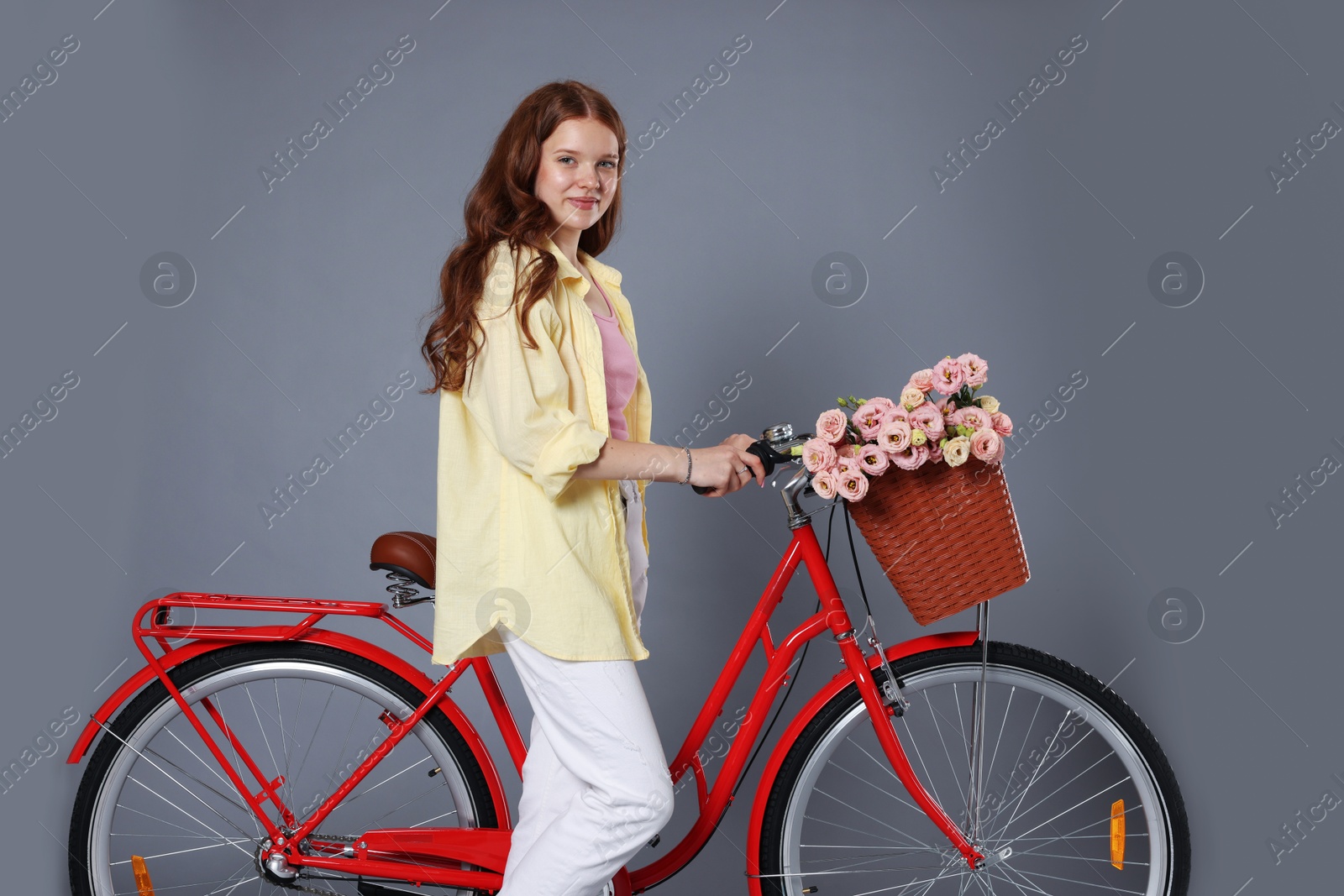 Beautiful teenage girl and bicycle with basket of flowers against grey background Photo of Beautiful teenage girl and bicycle with basket of flowers against grey background