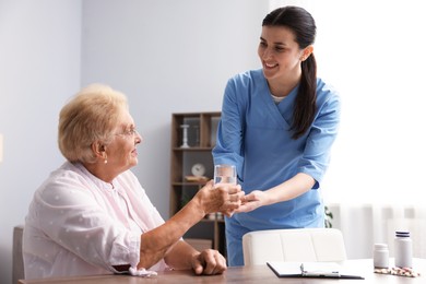 Photo of Nurse giving glass of water to senior woman indoors. Home health care service
