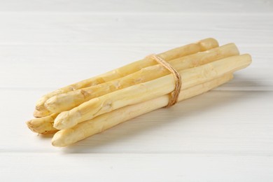 Photo of Bunch of raw asparagus spears on white wooden table, closeup