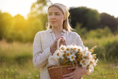 Photo of Happy woman with basket full of beautiful wildflowers outdoors