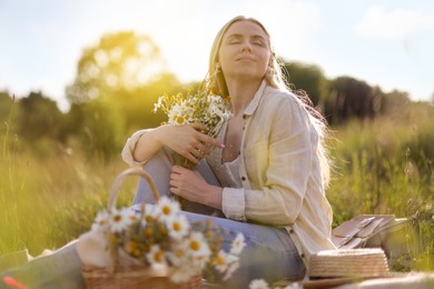 Photo of Beautiful woman with bouquet of wildflowers on blanket in meadow