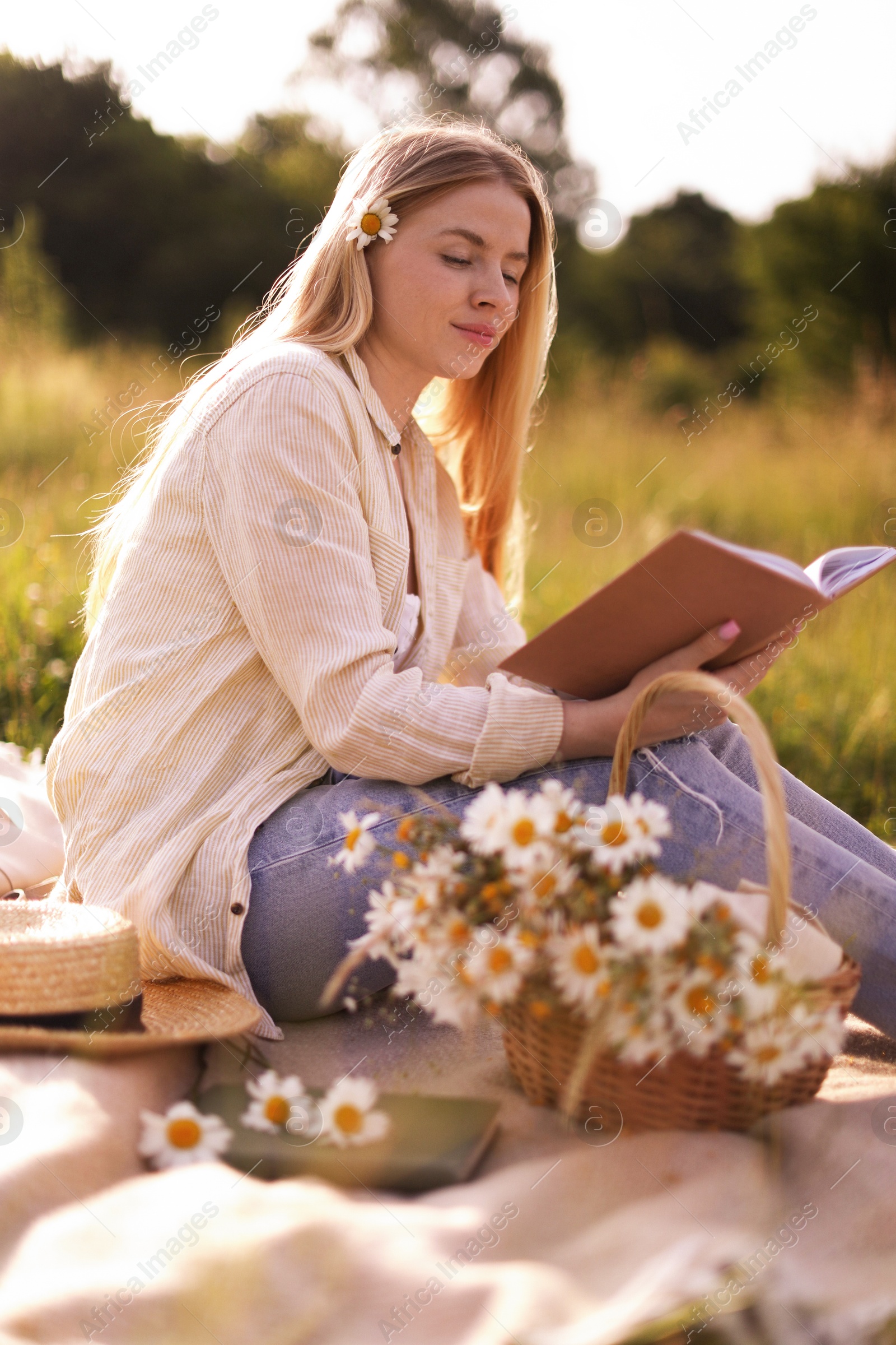 Beautiful woman with bouquet of wildflowers reading book on blanket in meadow Photo of Beautiful woman with bouquet of wildflowers reading book on blanket in meadow