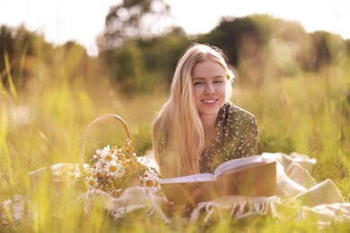 Photo of Beautiful woman with bouquet of wildflowers reading book on blanket in meadow