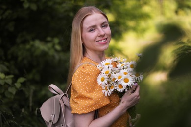 Photo of Beautiful woman with bouquet of wildflowers and backpack in forest