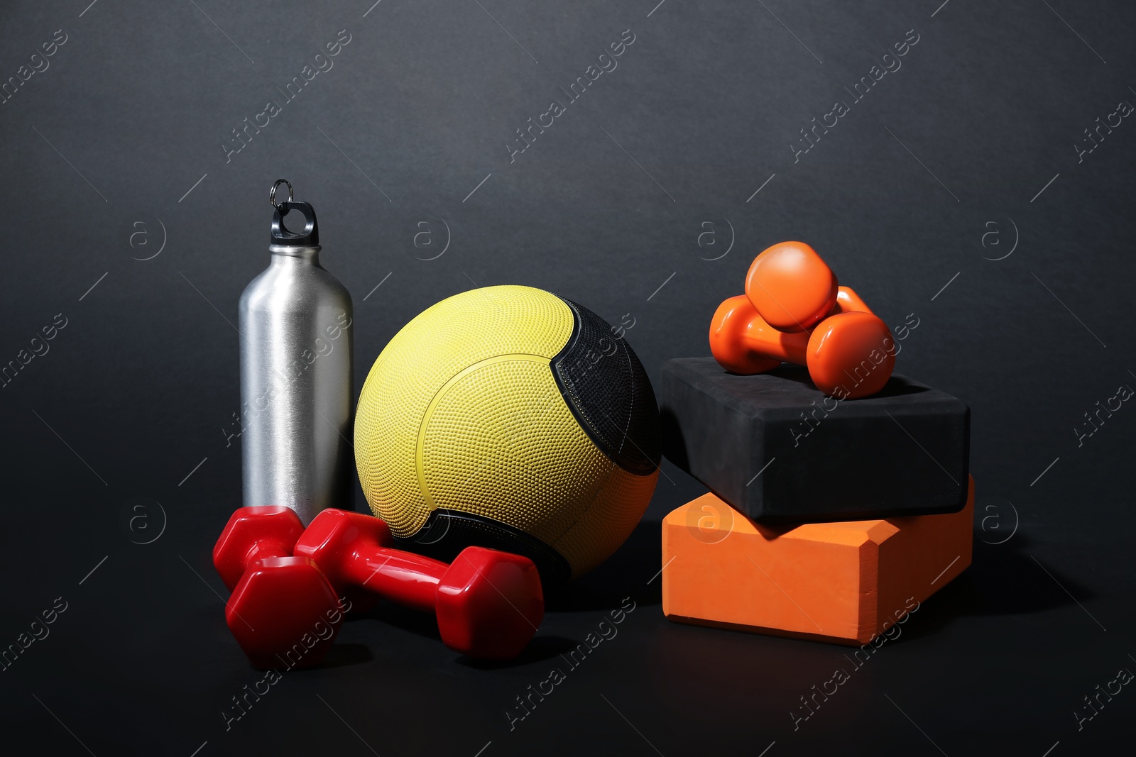 Medicine ball, dumbbells, foam blocks and water bottle on black background Photo of Medicine ball, dumbbells, foam blocks and water bottle on black background