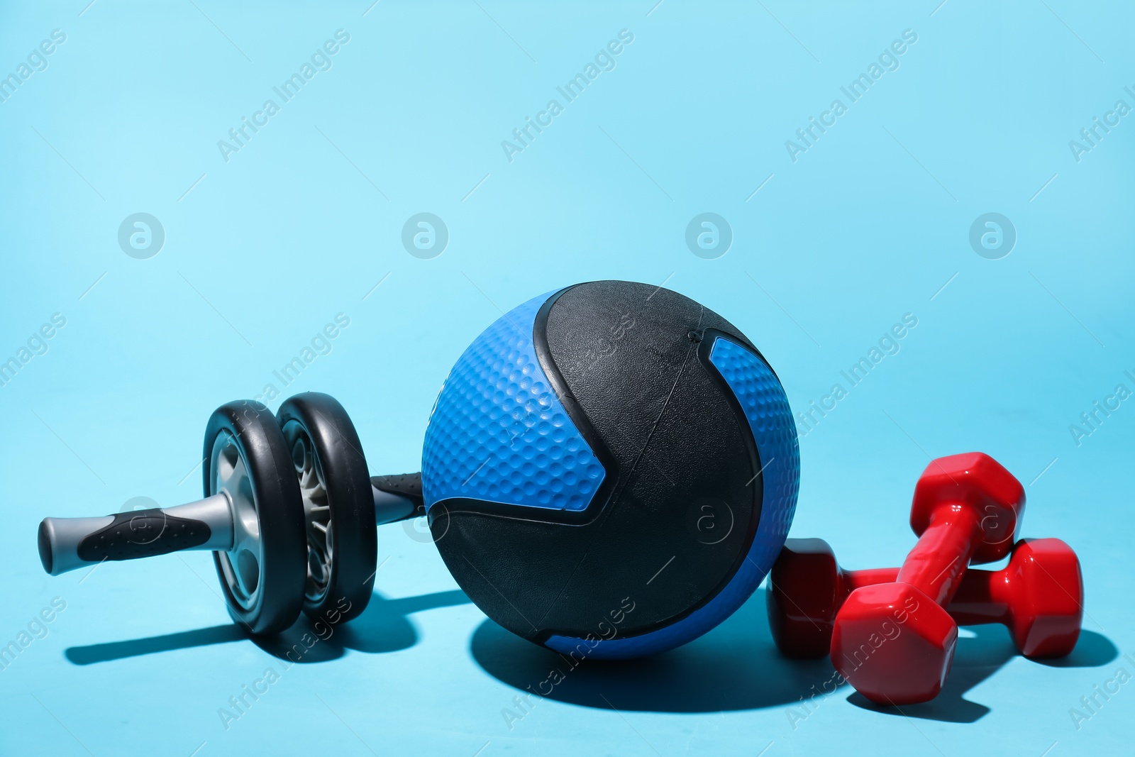 Photo of Medicine ball, ab wheel and dumbbells on light blue background