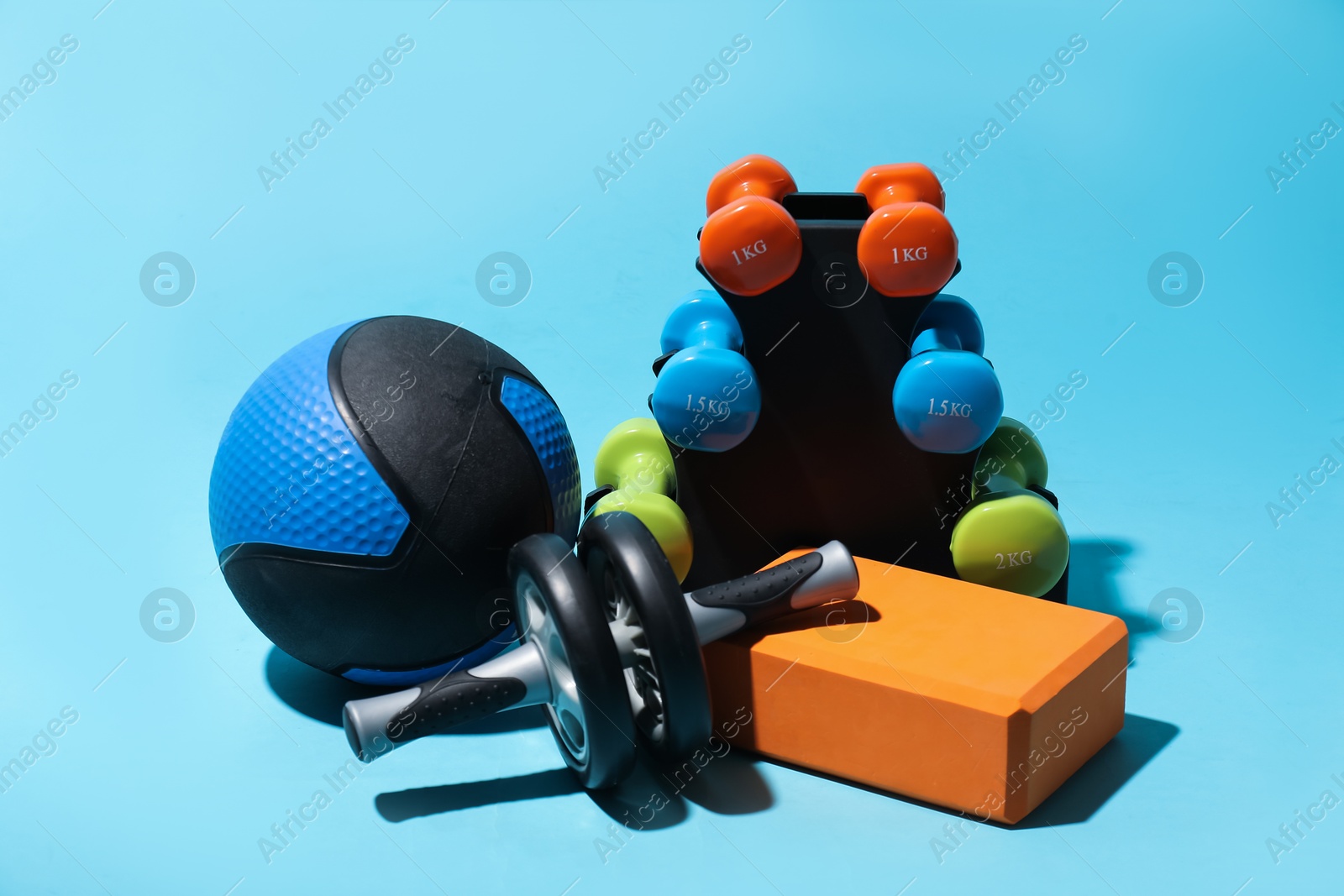 Medicine ball, ab wheel, foam block and dumbbells on light blue background Photo of Medicine ball, ab wheel, foam block and dumbbells on light blue background