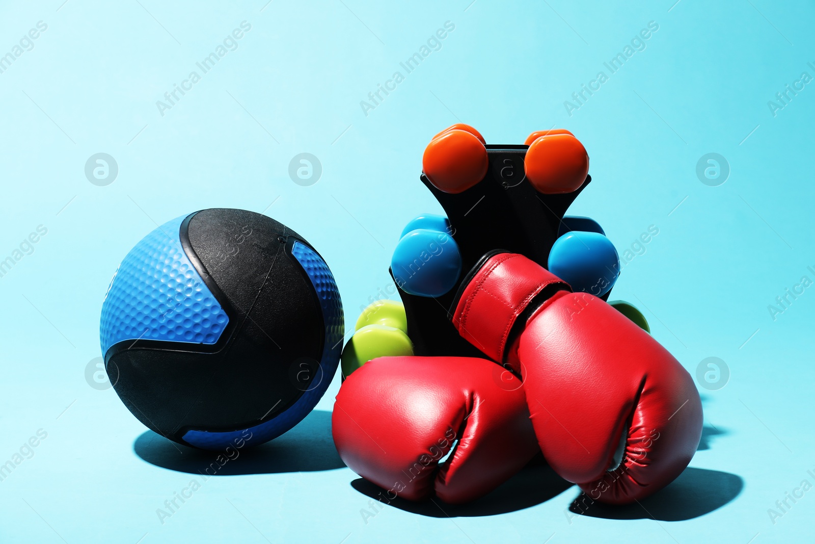 Medicine ball, dumbbells and boxing gloves on light blue background Photo of Medicine ball, dumbbells and boxing gloves on light blue background