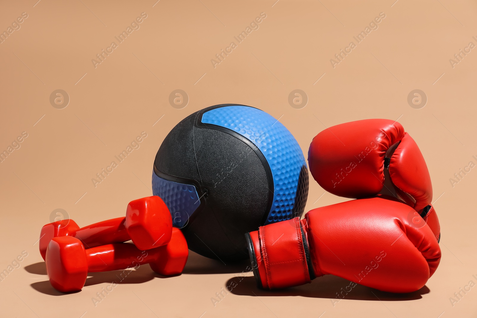 Photo of Medicine ball, dumbbells and boxing gloves on beige background
