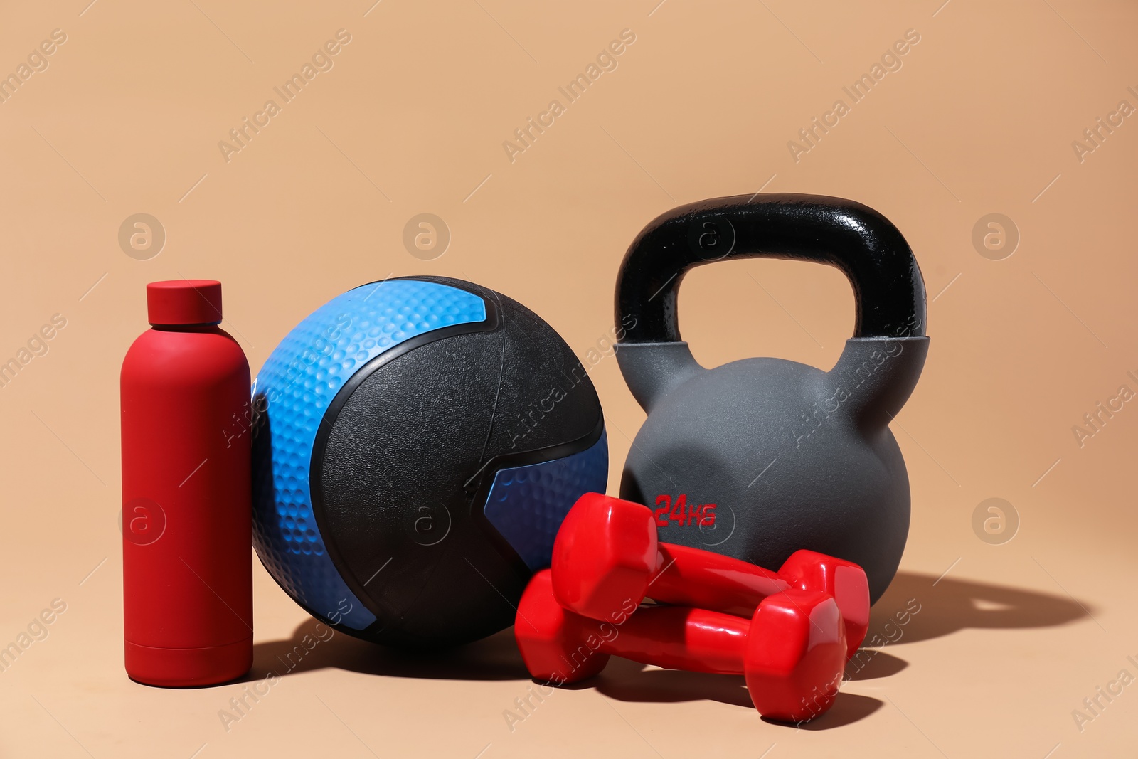 Photo of Medicine ball, dumbbells, water bottle and kettlebell on beige background