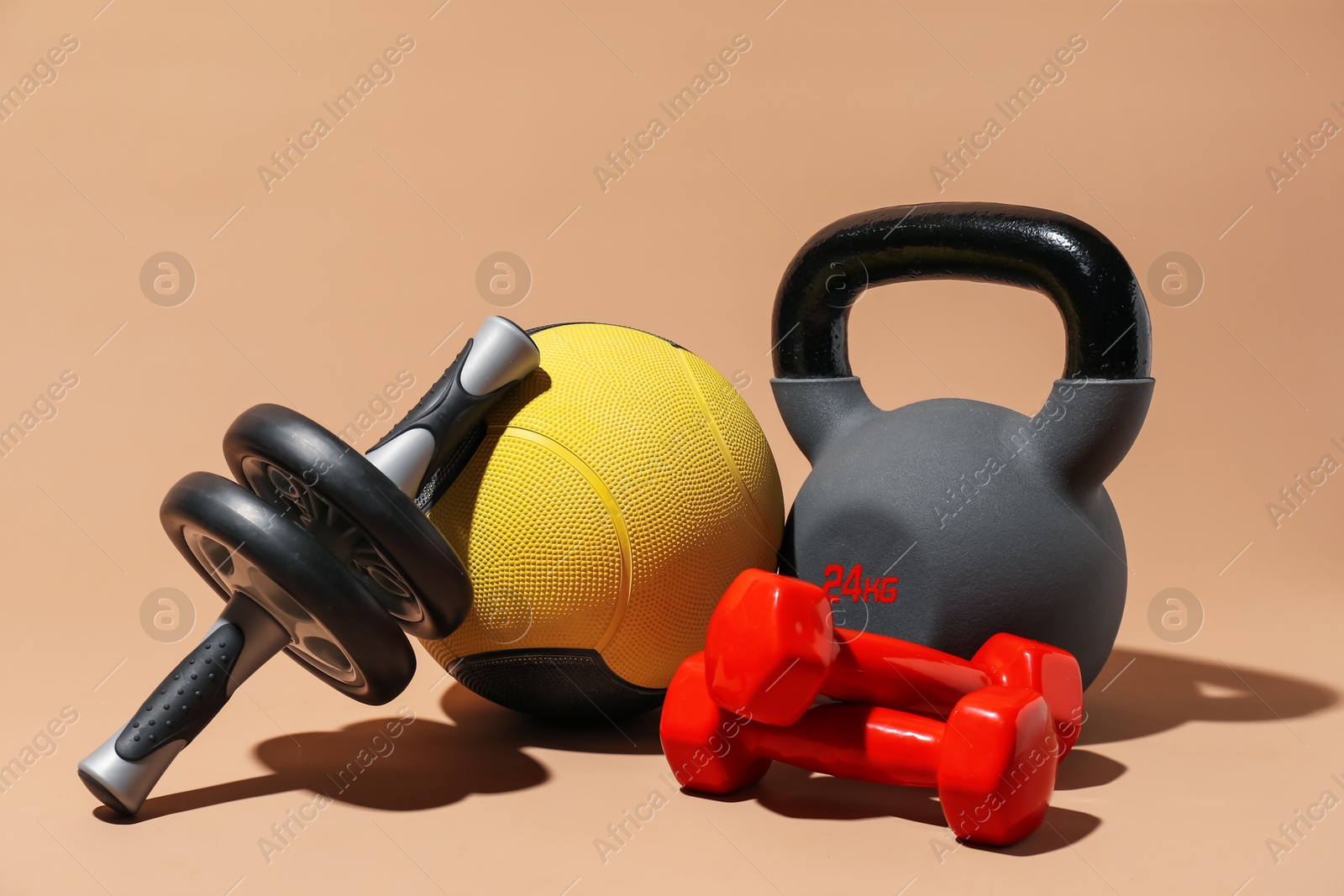 Medicine ball, dumbbells, ab wheel and kettlebell on beige background Photo of Medicine ball, dumbbells, ab wheel and kettlebell on beige background