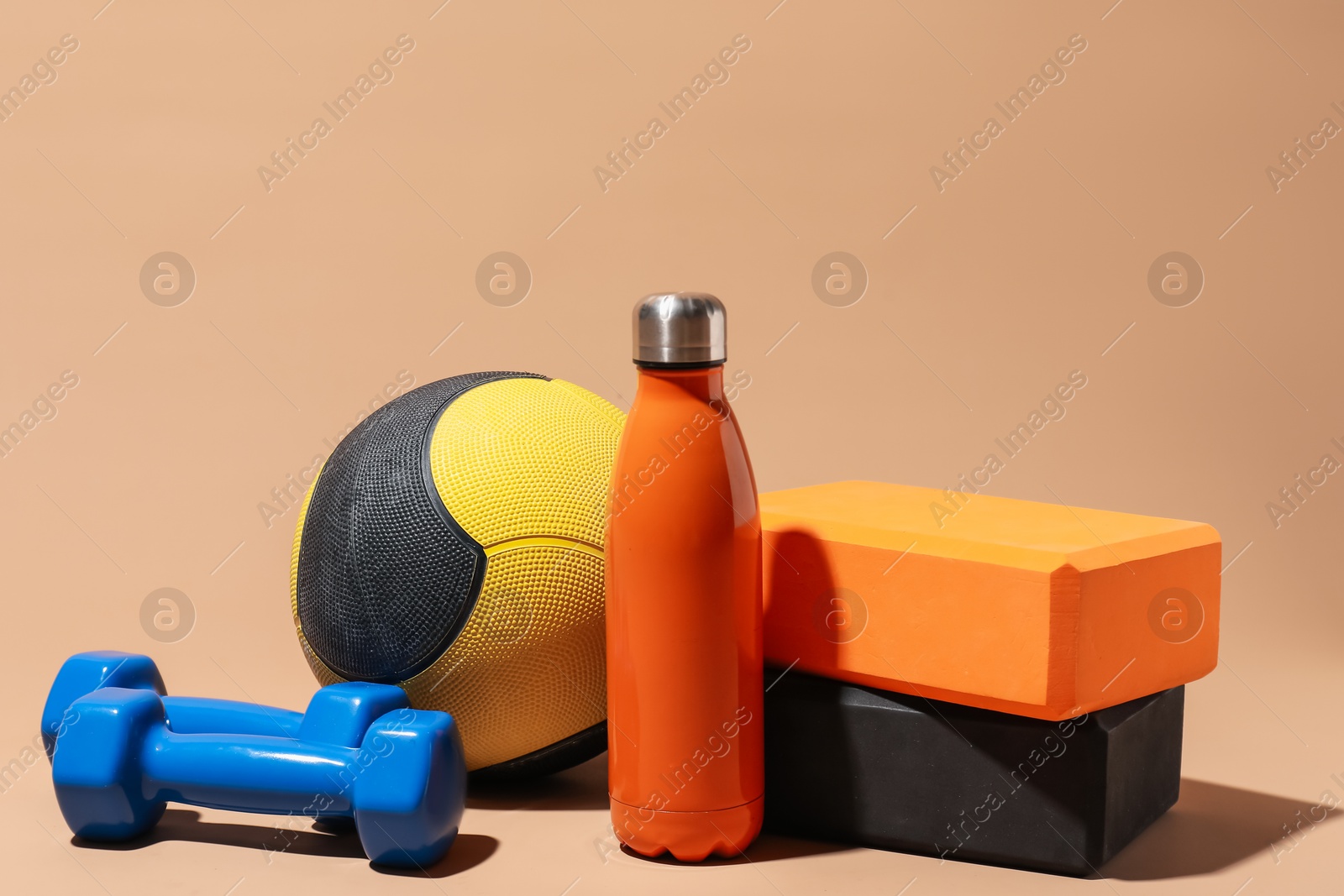 Medicine ball, foam blocks, dumbbells and water bottle on beige background Photo of Medicine ball, foam blocks, dumbbells and water bottle on beige background