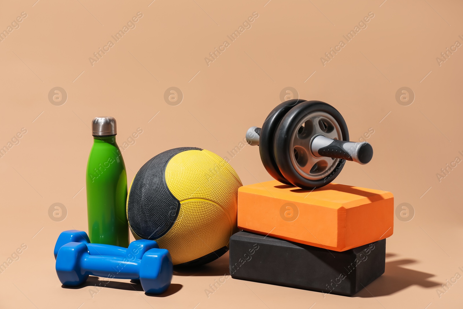 Photo of Medicine ball, foam blocks, dumbbells, ab wheel and water bottle on beige background