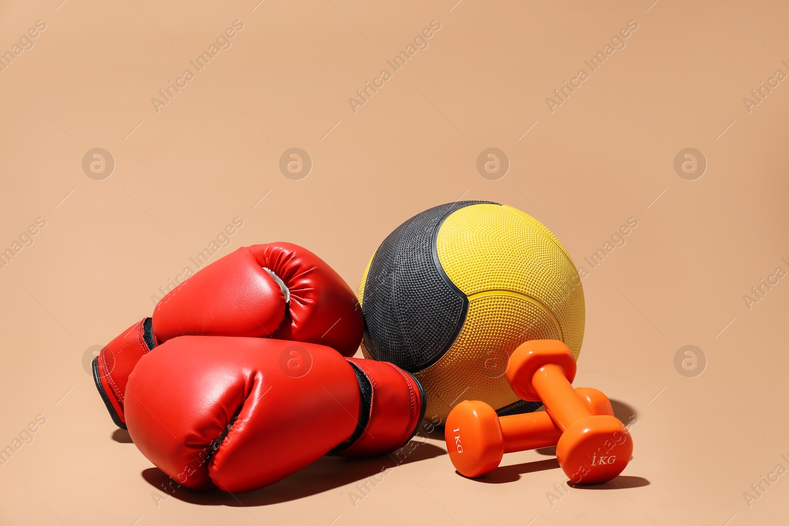 Photo of Medicine ball, dumbbells and boxing gloves on beige background