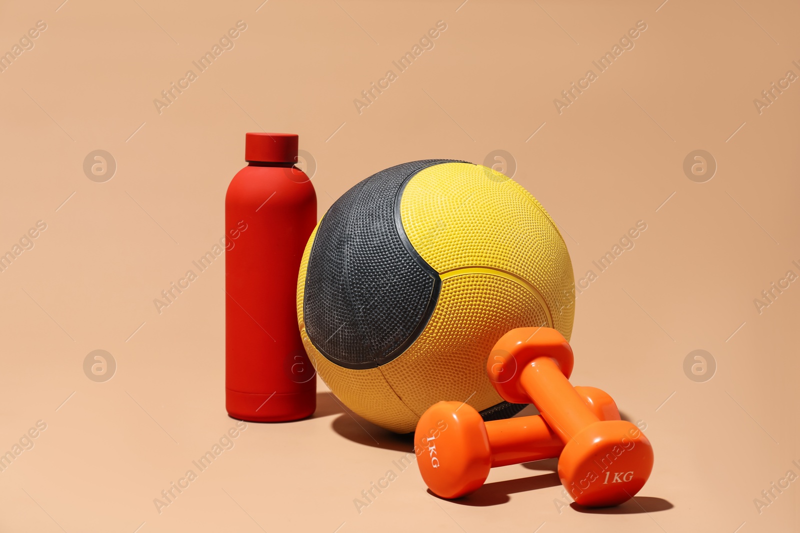 Medicine ball, dumbbells and water bottle on beige background Photo of Medicine ball, dumbbells and water bottle on beige background