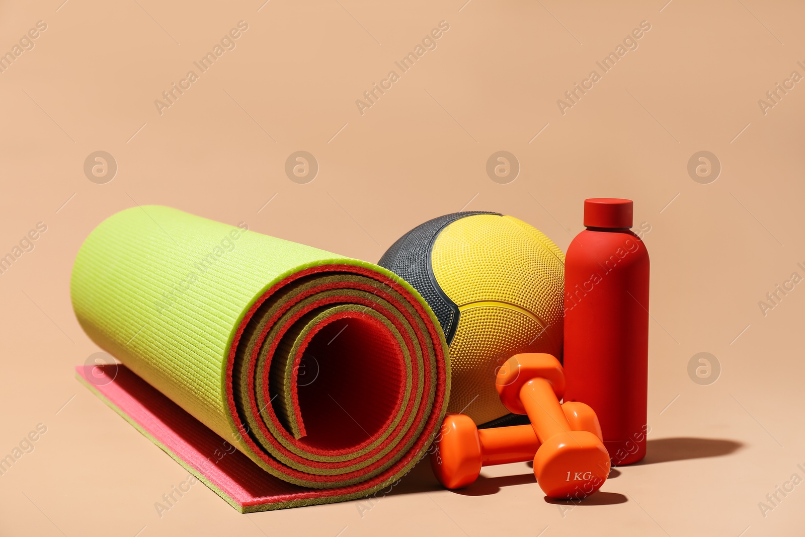 Medicine ball, dumbbells, fitness mat and water bottle on beige background Photo of Medicine ball, dumbbells, fitness mat and water bottle on beige background
