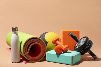Photo of Medicine ball, dumbbells, foam blocks, ab wheel, water bottle and fitness mat on beige background