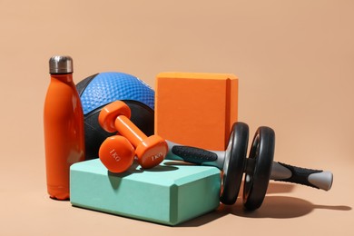 Photo of Medicine ball, dumbbells, foam blocks, ab wheel and water bottle on beige background