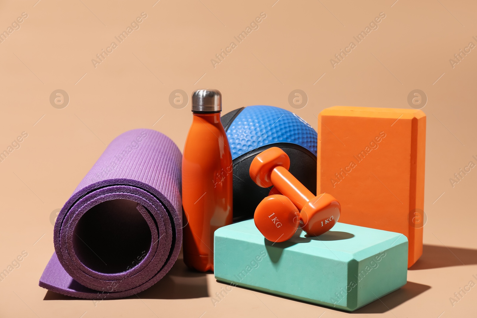 Photo of Medicine ball, fitness mat, dumbbells, foam blocks and water bottle on beige background
