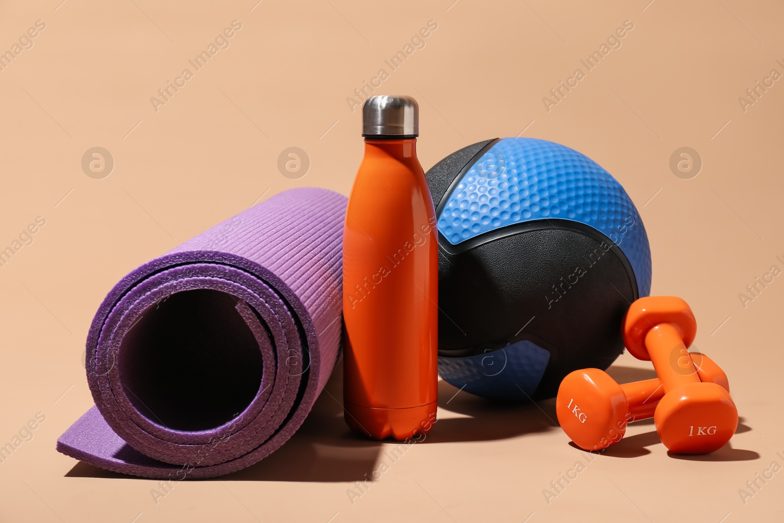 Medicine ball, fitness mat, dumbbells and water bottle on beige background Photo of Medicine ball, fitness mat, dumbbells and water bottle on beige background