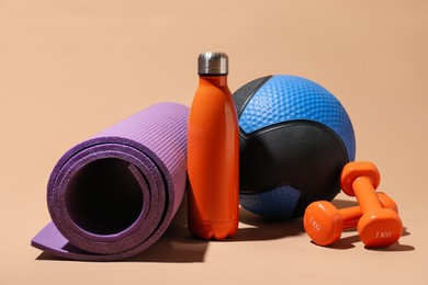 Photo of Medicine ball, fitness mat, dumbbells and water bottle on beige background