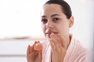 Photo of Young woman with lip balm at home, space for text